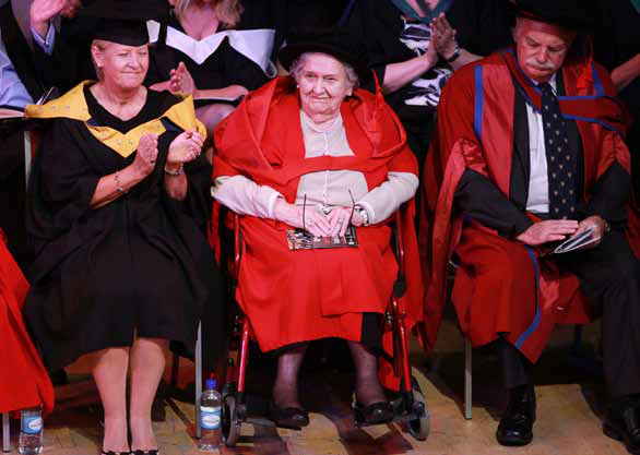 Honorary Fellow Margaret Thorne on stage in wheelchair in graduation robes.
