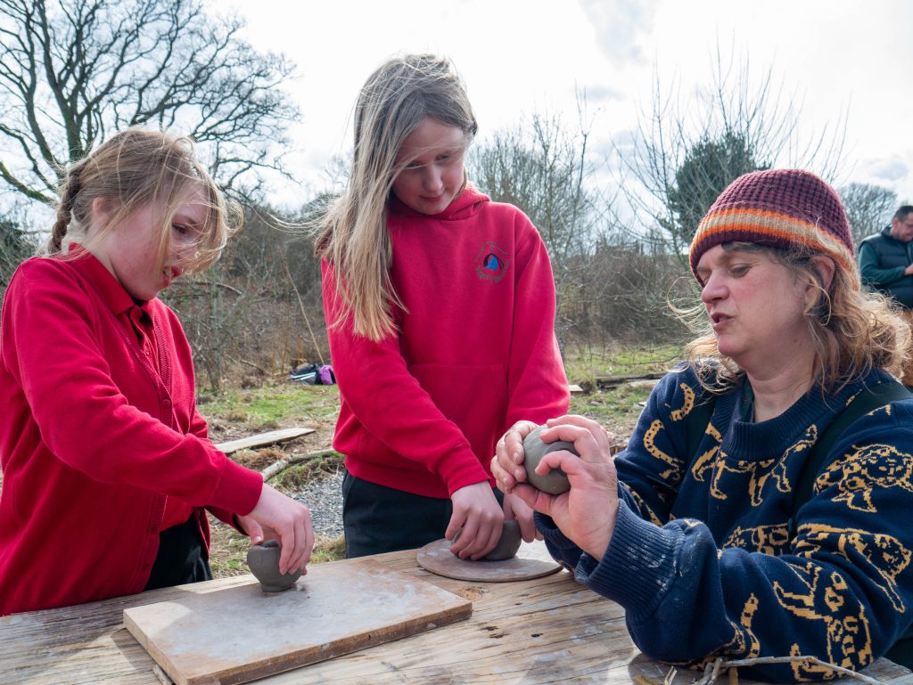 Two young female students and a nature worker moulding clay pots.