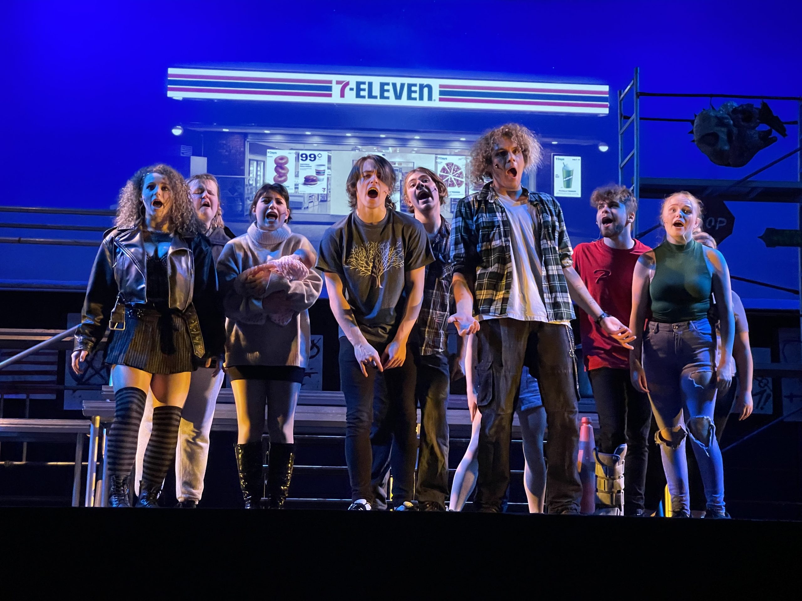 Newtown College students on stage with a 7-Eleven in the background, performing American Idiot