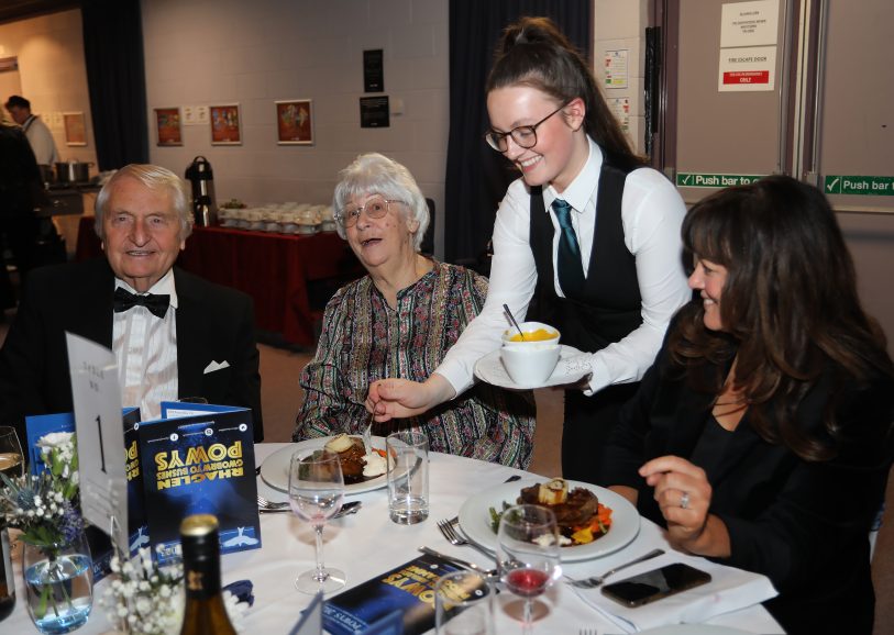 A Catering & Hospitality student at Newtown College dressed formally, serving guests at a table at the Powys Business Awards