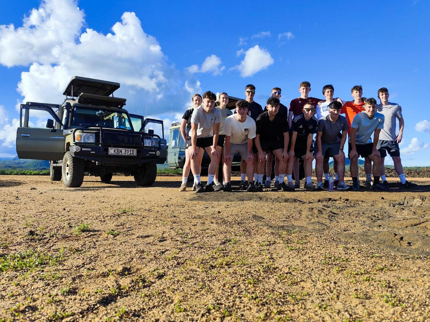Sports students in a group photo on a safari next to a jeep.